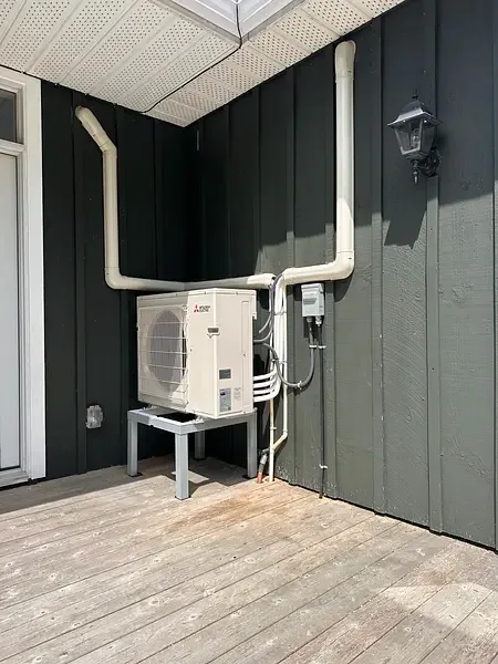 Ductless heat pump outdoor unit installed on a stand beside a cottage deck by Burt's Breeze