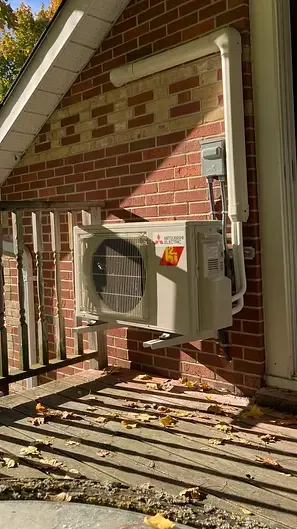 Mini-split condenser neatly wall-mounted on a brick home by Burt's Breeze